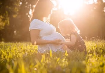kobieta w ciąży z dziewczynką na łące 