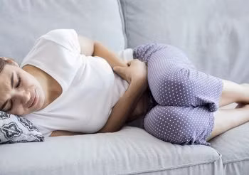 Młoda kobieta leżąca w skulonej pozycji na kanapie