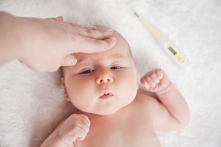 Mama dotyka ręką czoła niemowlęcia z objawami gorączki