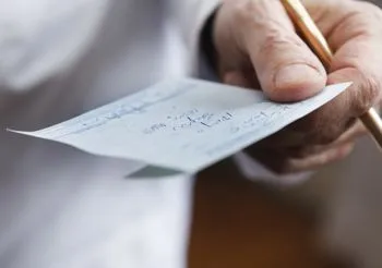 Zbliżenie na dłoń farmaceuty, trzymającego receptę. 