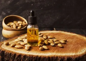 Olej z migdałów w buteleczce z pipetką i migdały rozsypane na pniu drzewa 