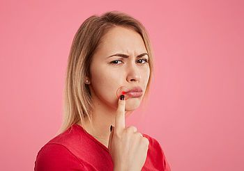 Młoda kobieta niezadowolona wskazuje palcem na kącik ust