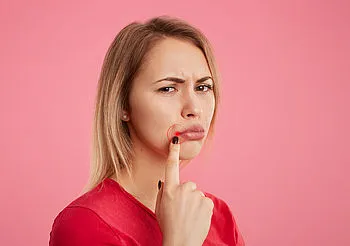 Młoda kobieta niezadowolona wskazuje palcem na kącik ust 