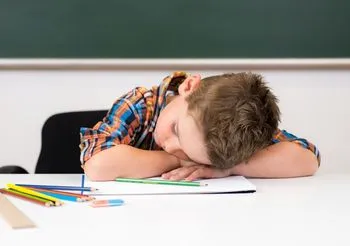 chłopiec opiera się o ławkę szkolną i drzemie na otwartym zeszycie