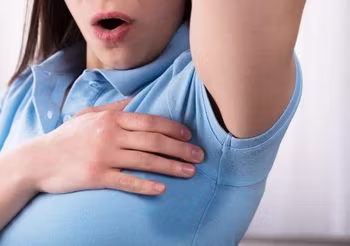 Kobieta z podniesioną ręką i mokra plamą na bluzce pod pachą