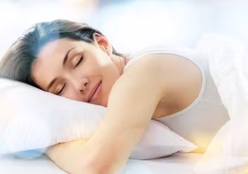 Odprężeona młoda kobieta w jasnej pościeli. 