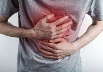 Grafika przedstawia mężczyznę trzymającego się za brzuch, który cierpi na refluks. 