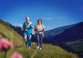 starsza para maszeruje szlakiem górskim z kijkami do nordic walking