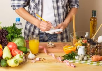 mężczyzna przygotowuje listę zakupów w kuchni pełnej owoców i warzyw