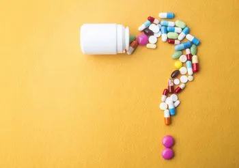 Znak zapytania ułożony z kolorowych tabletek na żołtym tle 