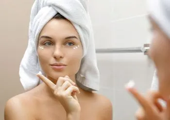 Młoda kobieta nakladająca krem na skóre twarzy 