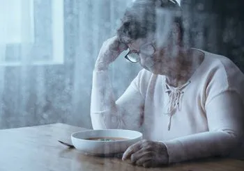 Smutna starsza kobieta siedząca nad talerzem zupy