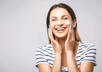 Młoda kobieta wklepująca w policzki krem 