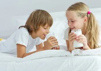 Dzieci leżące w łóżku i pijące kefir