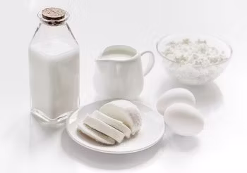 na obok siebie na białej powierzchni stoją butelka mleka, dzbanuszek ze śmietaną, twaróg, ser i jaja