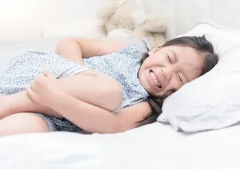 Dziewczynka leżąca na łóżku i trzymająca się za brzuch