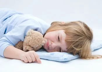 Kilkuletnia dziewczyna leży w łóżku z misiem i nie może zasnąć