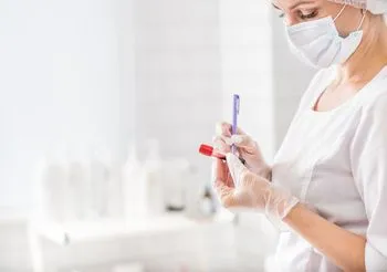 kobieta w maseczce i ubraniu ochronnym opisuje próbkę krwi w laboratorium