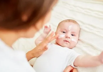 Młoda mama smarująca noworodka kremem ochronnym