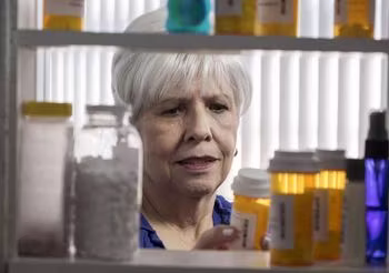 starsza kobieta wybiera lekarstwa z szafki na leki