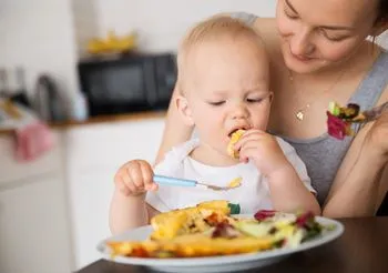 Kielkumiesięczne dziecko je obiad siedząc i mamy na kolanach 