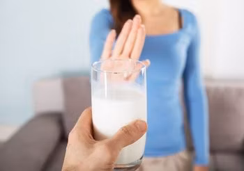kobieta odpycha ręką podsuwaną jej szklankę mleka