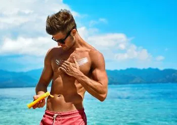 Młody mężczyzna smaruje się filtrem na plaży