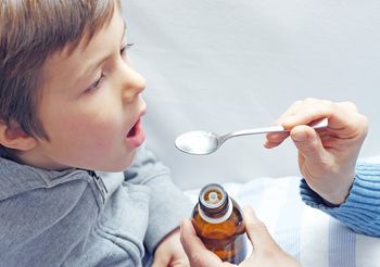 Kilkuletni chłopiec, któremu rodzić podaje syrop. 